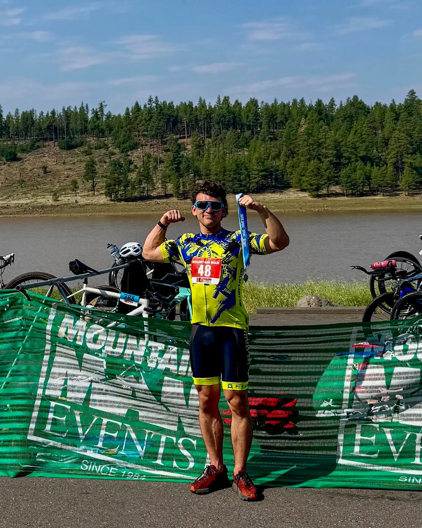 Athlete in a colorful outfit with a number 48 posing in front of a green banner with 'Mountain Triathlon Events' text.
