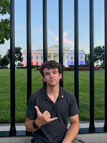 Person making a hand gesture in front of a fence with the White House in the background